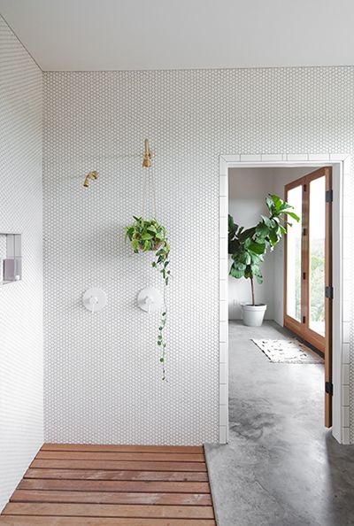 concrete floors, open shower with wood floor, walls of mini white hexagon tile, doorway framed in white subway tile